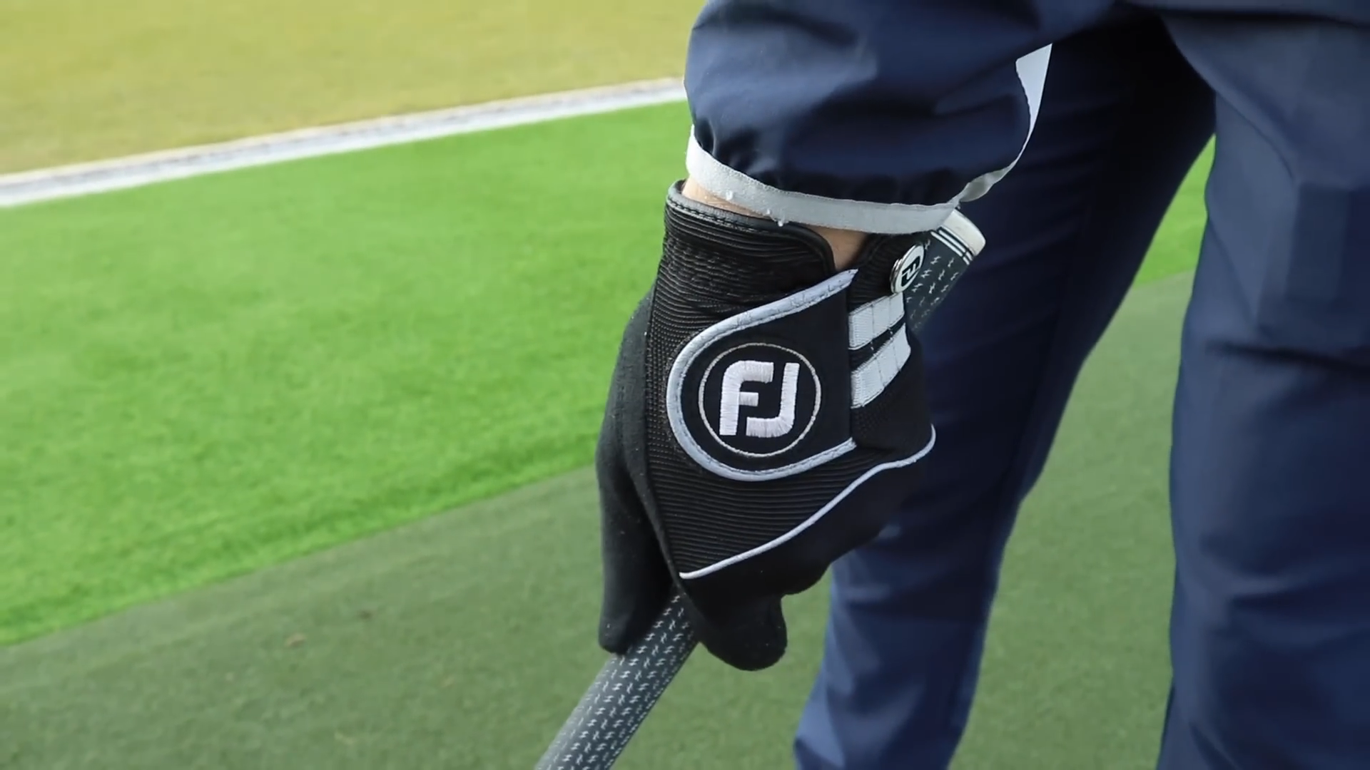 Golf Gloves in Use, Showing a Black Design with Fj Logo, Gripping a Golf Club on A Green Course