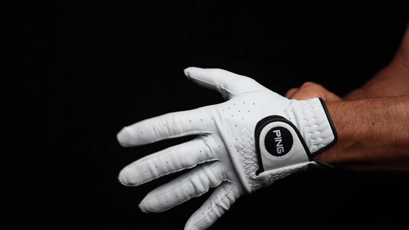 PING Tour Golf Glove, White with Black Accents, Worn on Hand Against a Dark Background